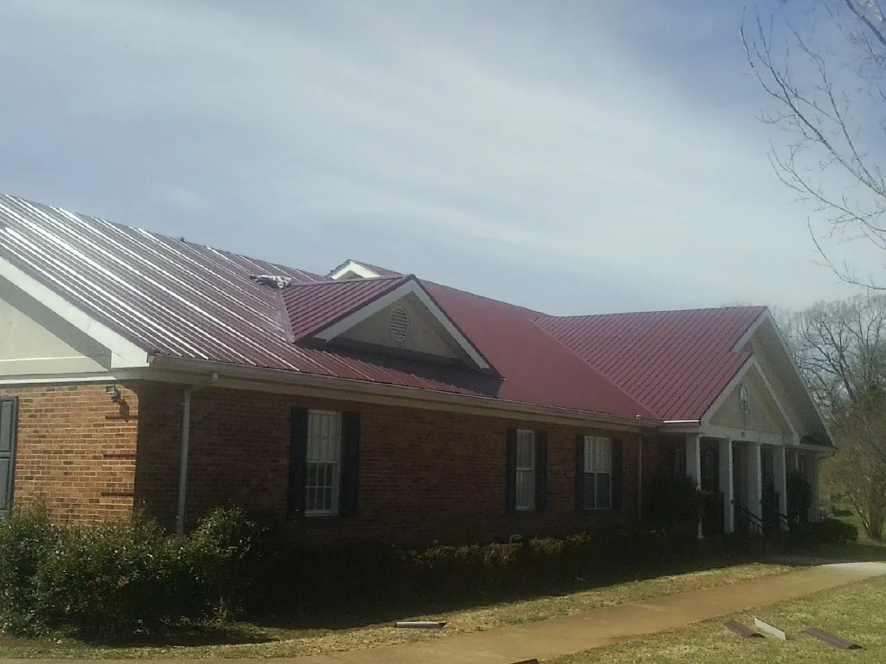 Red metal roof with gabled entries on a long brick building, from a Hail Damage Roof Repair job in Pontiac
