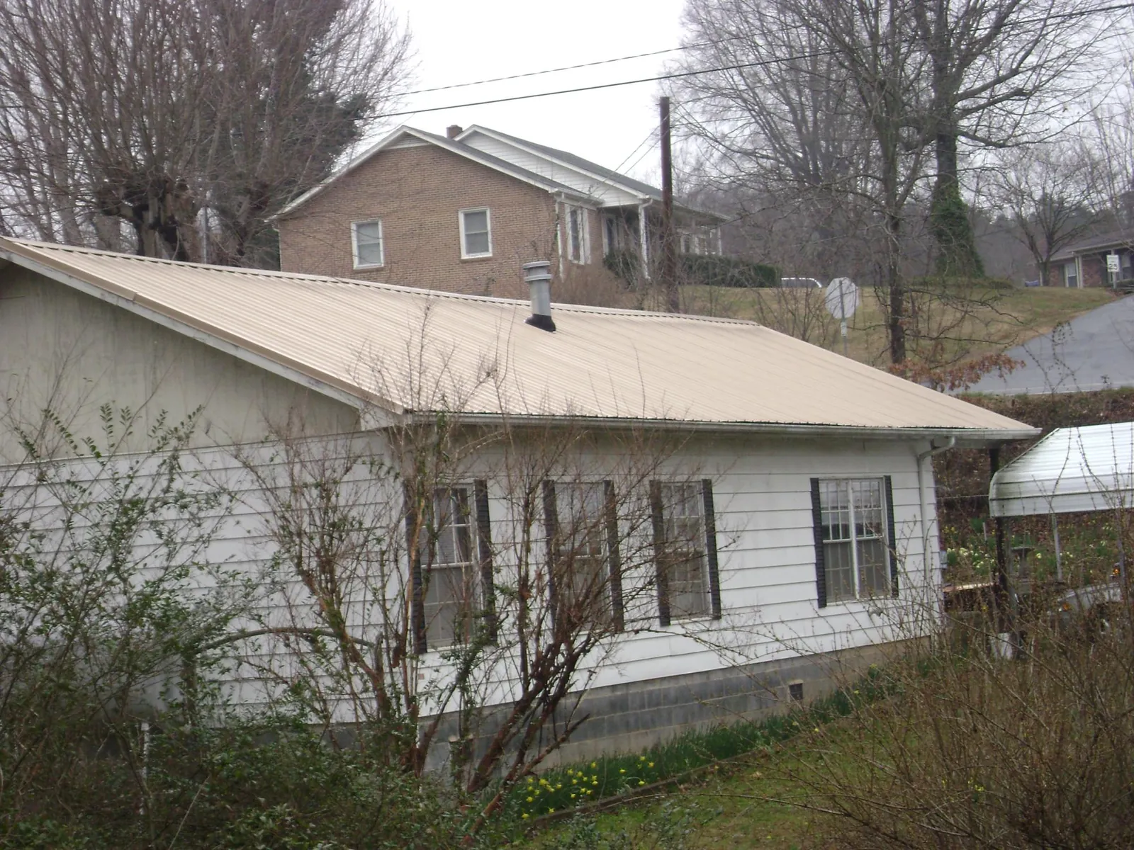Tan metal roof on a white sided house set into a hillside — Commercial Roofing by Roofing Brothers in Pontiac